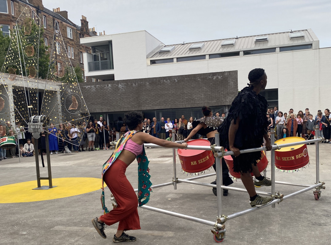 Performers pushing a scaffolding float within a courtyard, Ashanti Harris exhibition